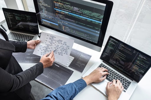 Two professionals engage with laptops, highlighting the difference between help desk vs. service desk.