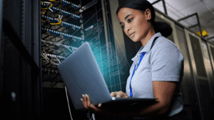 Image of a person using a laptop near a server stack
