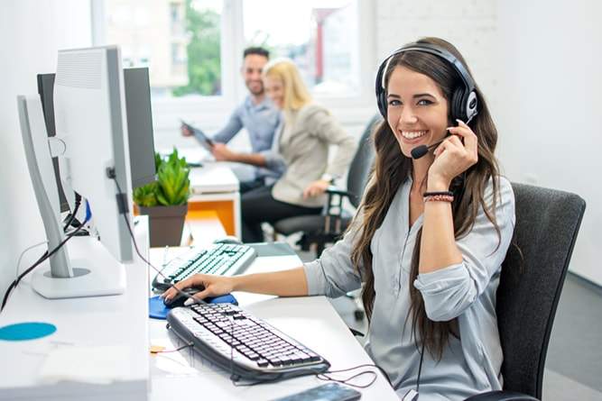  HDI-certified IT help desk team and a smiling woman in an office with headphones, demonstrating effective help desk best practices.