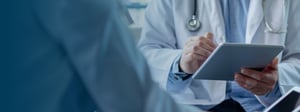 Doctor in a clinical setting using a tablet to review patient information during a consultation, representing digital healthcare technology and electronic records.