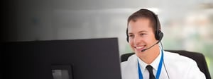 Smiling IT support professional wearing a headset and working at a computer, representing remote IT support services.