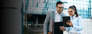 Two business professionals reviewing information on a tablet and clipboard outside a modern office building, discussing service level agreements and performance expectations.