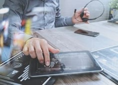 Hands interacting with a tablet displaying data dashboards on a desk, symbolizing business analytics, IT oversight, and managed services support.