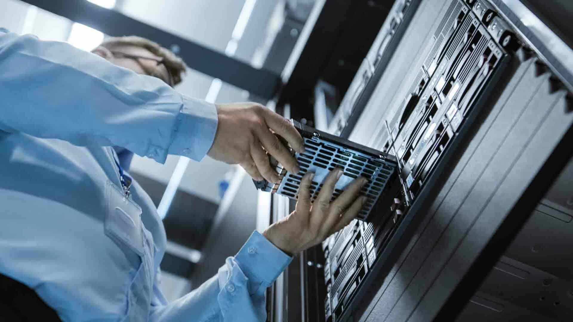 A technician installs a server component into a rack-mounted system inside a data center, illustrating on-premises IT infrastructure and hardware maintenance.