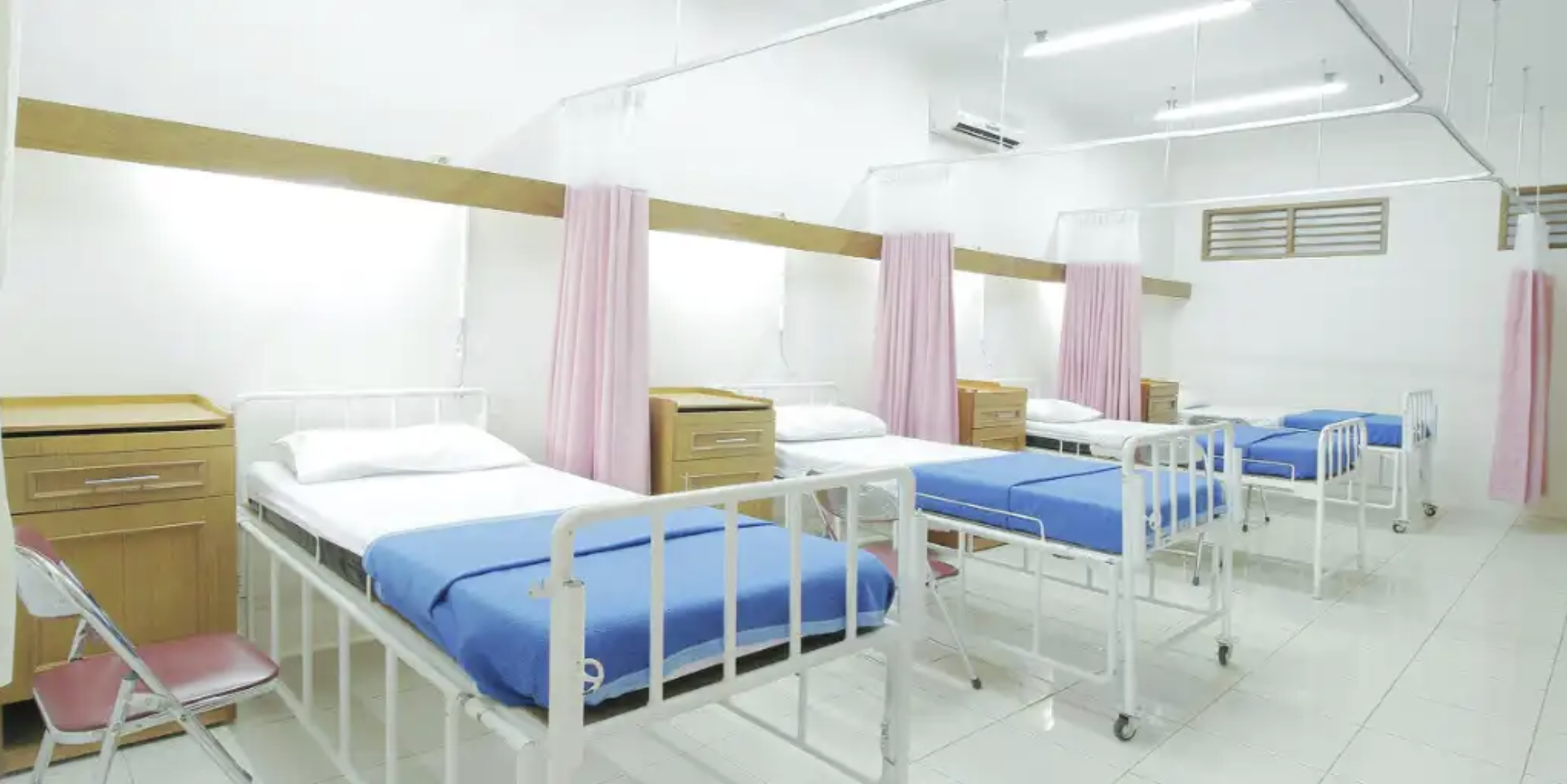 A bright hospital ward with multiple patient beds separated by curtains, showing a shared inpatient care environment supported by hospital services.